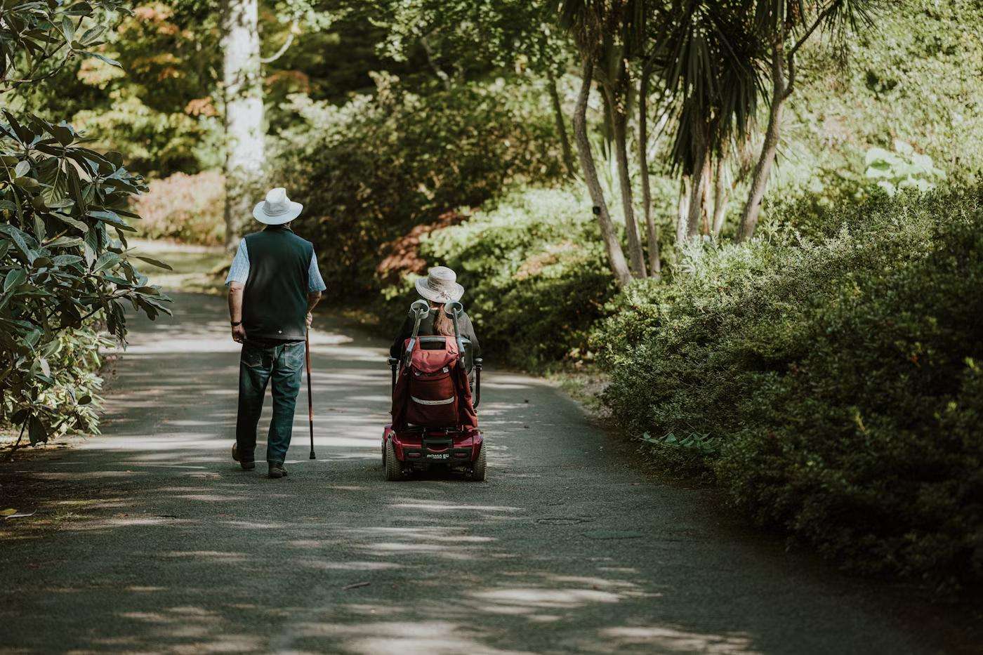 man walking with cane next to partner in motorised wheelchair